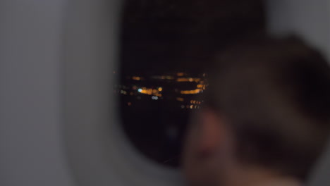 Niño-Mirando-La-Ciudad-De-Noche-Desde-Un-Avión-Volador