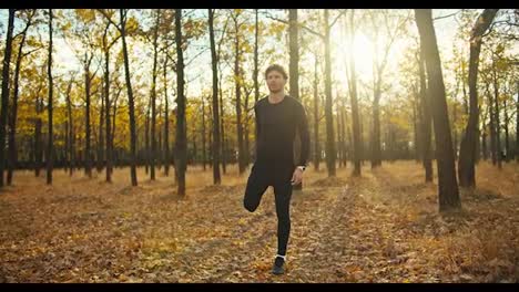 A-confident-and-serious-man-with-curly-hair-in-a-black-sports-uniform-is-warming-up-and-then-looking-at-his-watch-and-starting-his-jog-in-the-morning-autumn-forest-in-autumn