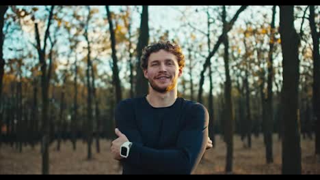 Portrait-of-a-happy-and-confident-man-with-curly-hair-a-brunette-with-a-beard-who-crossed-his-arms-on-his-chest-and-stands-confidently-while-jogging-in-the-autumn-forest-in-the-morning