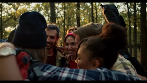 a-happy-group-of-friends-in-hiking-clothes-hugging-in-a-circle-and-enjoying-their-company.-A-small-group-rejoices-while-hiking-in-the-summer-forest