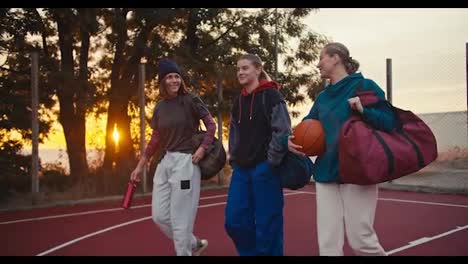 A-happy-company-of-girls-basketball-players-walk-along-the-basketball-field-with-a-ball-in-their-hands-and-communicate-early-in-the-morning-at-Sunrise