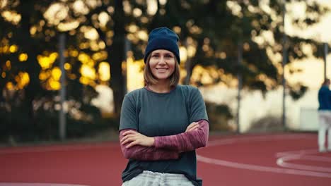 Portrait-of-a-happy-blonde-girl-with-a-bob-hairstyle-in-a-gray-sports-uniform-who-looks-at-the-camera-and-smiles-on-a-street-area-early-in-the-morning-at-sunrise