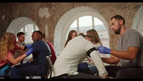 Entrenamiento-Práctico-De-Habilidades-Laborales-Con-Arneses-Médicos.-Una-Niña-Aprieta-Un-Torniquete-Médico-En-La-Mano-De-Un-Asistente-Masculino-Negro-Con-Uniforme-Médico-Azul.