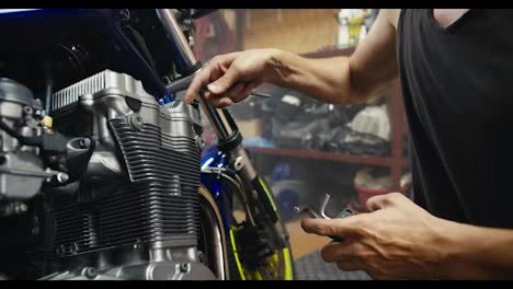 Close-up-shot-of-a-man-using-his-strong,-sinewy-hands-to-tighten-a-nut-and-repair-a-motorcycle-using-a-hex-tool-in-his-garage-workshop