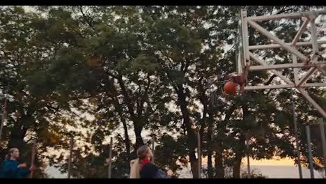 A-blonde-girl-throws-a-basketball-into-the-basket-and-scores-a-goal-on-a-red-basketball-court-while-playing-with-her-friend-at-Sunrise-in-the-morning