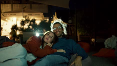 Close-up-shot:-a-couple-in-love-are-lying-on-beanbag-chairs-and-watching-a-movie.-A-party-outside-the-city.-Rest-in-the-country-house