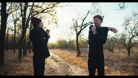 a-man-with-curly-hair-and-a-beard-in-a-black-sports-uniform-together-with-his-friend-in-a-red-cap-are-doing-sports-and-warming-up-before-jogging-in-an-autumn-park-in-the-morning