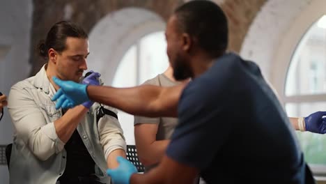 A-group-of-people-perform-practical-exercises-in-medicine-for-first-aid-under-the-supervision-of-a-professional-black-male-doctor-against-the-background-of-large-windows.-Course-of-a-medic