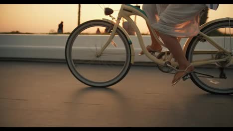 Una-Niña-Con-Un-Vestido-Blanco-Pedalea-Una-Bicicleta-Y-Pasea-Por-La-Playa-Durante-El-Amanecer-Cerca-Del-Mar.-Paseo-En-Bicicleta-Por-La-Mañana-Hasta-La-Playa-Cerca-Del-Mar-Donde-Crecen-Palmeras.