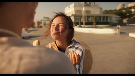 Close-up-shot-of-a-brown-haired-girl-in-a-white-blue-shirt-eating-a-hot-dog-in-the-summer-on-a-modern-beach-in-the-morning