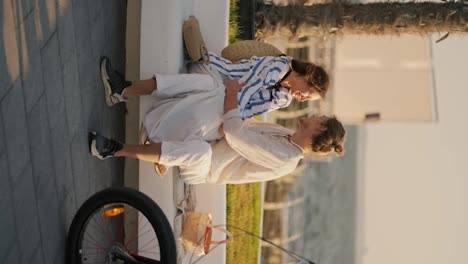 Vertical-video-of-a-guy-and-a-girl-in-beachwear-sitting-on-a-white-bench-on-a-modern-beach-and-talking-on-their-date-near-the-sea.-Happy-couple-on-a-date-on-a-pier-near-the-sea