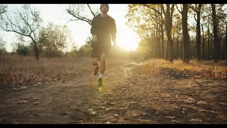 Un-Atleta-Masculino-Con-Gorra-Roja-Y-Uniforme-Deportivo-Negro-Se-Agarra-La-Rodilla-Y-Cae-Al-Suelo-Mientras-Corre-Porque-Se-Lesionó-La-Pierna-Por-La-Mañana-En-El-Bosque-Otoñal-Al-Amanecer.