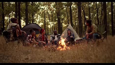 Cheerful-and-happy-participants-of-a-group-hike-in-plaid-shirts-sit-near-a-fire-and-enjoy-their-company-during-a-hike-in-a-yellow-autumn-forest