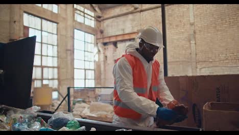 A-man-with-Black-skin-in-a-white-uniform-and-an-orange-vest-in-protective-blue-gloves-sorts-through-garbage-and-plastic-bottles-depending-on-color-at-the-Large-Waste-Recycling-Plant