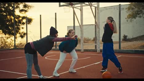 Un-Trío-De-Atletas-Femeninas-Y-Jugadoras-De-Baloncesto-Vestidas-Con-Ropa-Deportiva-Se-Calientan-En-Una-Cancha-Deportiva-Roja-Para-Jugar-Al-Baloncesto-Cerca-De-Una-Pelota-Naranja-Temprano-En-La-Mañana.