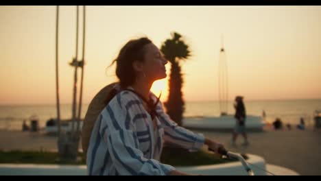 Happy-brunette-girl-in-a-striped-shirt-rides-a-bicycle-along-the-sea-on-the-beach-in-the-morning-at-dawn.-Morning-bike-ride-on-the-beach-at-sunrise