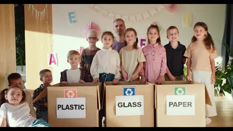 portrait-of-happy-children-together-with-their-teacher-near-special-boxes-for-sorting-garbage-in-the-clubhouse-for-preparing-children-for-school.-portrait-of-a-group-of-children-learning-to-sort-garbage