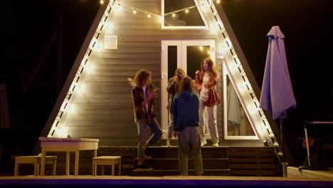 A-company-of-two-boys-and-two-girls-dance-together-against-the-background-of-glowing-lights.-Resting-at-a-party-outside-the-city.-Rest-in-the-country-house