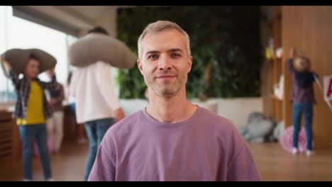 Retrato-De-Un-Hombre-Feliz-Con-Cabello-Gris,-Profesor-Con-Una-Camiseta-Morada-Que-Posa-Y-Mira-A-La-Cámara-Durante-Un-Descanso-En-Un-Club-De-Preparación-Escolar-Para-Niños.