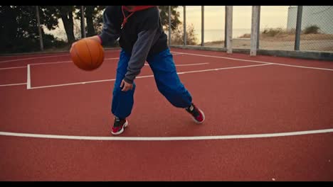 Close-up-Portrait-a-blonde-girl-in-blue-pants-hits-the-ball-and-then-poses-and-looks-at-the-camera-during-her-morning-practice-on-the-red-basketball-court-in-the-morning