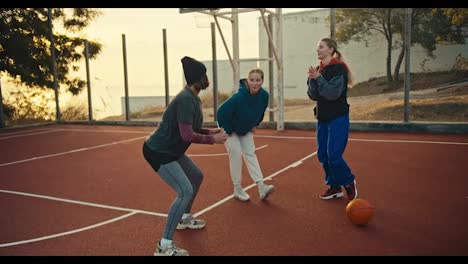 Close-up-of-a-blonde-girl-in-a-bob-hairstyle-in-a-black-hat-in-a-sports-uniform,-together-with-her-two-friends,-warming-up-before-playing-basketball-with-an-orange-sword-on-a-red-court-at-dawn-in-the-morning