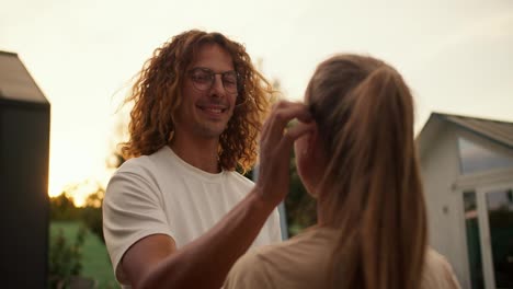 A-curly-haired-guy-in-glasses-fixes-his-girlfriend's-hair-and-hugs-her.-Rest-in-the-country-house