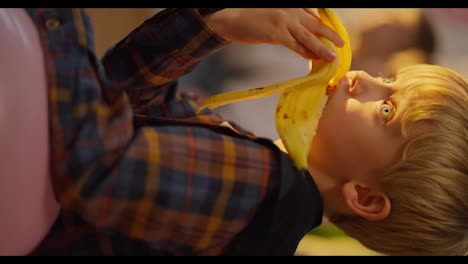 Vertical-video-shooting-close-up-of-a-stole-boy-with-blue-hair-eating-a-banana-during-a-break-and-lunch-in-a-club-for-preschool-children-in-a-sunny-cozy-room