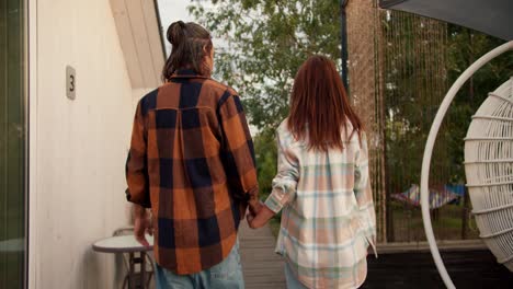 Shooting-from-behind:-A-red-haired-girl-with-her-long-haired-brunette-boyfriend-in-a-white-checkered-shirt-are-walking.-Rest-in-the-country-house