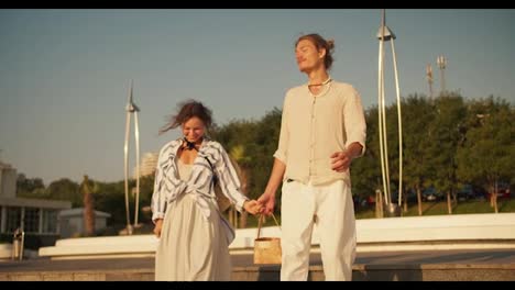 A-guy-and-a-girl-hold-hands-and-carry-a-basket-and-go-to-the-beach-together-on-a-date.-Happy-guy-and-girl-went-out-to-the-beach-with-palm-trees-during-a-date