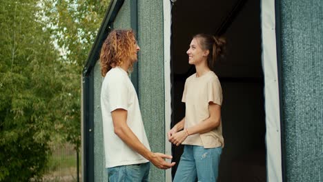 A-guy-with-curly-hair-in-a-white-t-shirt-is-talking-to-his-girlfriend-outside.-The-girl-fixes-her-boyfriend's-hair-and-smiles.-Rest-in-the-country-house