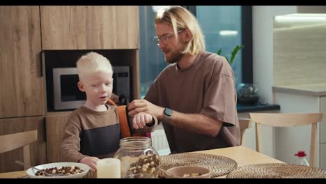 Ein-Blonder-Mann-Mit-Bart-Und-Brille-Legt-Seinem-Kleinen-Albino-Sohn-Mit-Weißen-Haaren-Einen-Leuchtend-Roten-Rucksack-An-Und-Sagt-Ihm-Nette-Worte,-Bevor-Ein-Neuer-Schultag-In-Der-Schule-Beginnt