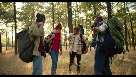 A-group-of-people-in-special-hiking-clothes-pick-up-their-hiking-backpacks-and-begin-to-move-through-the-sunny-summer-forest.-The-end-of-the-camping-trip-and-the-beginning-of-a-new-path