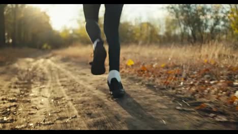 Close-up-a-man-in-a-black-sports-uniform-and-black-sneakers-runs-along-an-earthen-path-in-the-autumn-forest-among-fallen-brown-leaves-and-dry-grass-in-the-fall