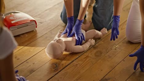 Close-up-shooting:-a-blonde-girl-in-jeans-learns-to-do-artificial-respiration-with-a-mannequin-baby-under-the-instructions-of-a-professional-nurse-girl-in-a-white-medical-uniform