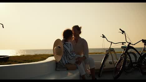 Happy-couple-in-love:-a-blond-guy-and-a-brown-haired-girl-with-a-Straw-hat-who-sits-on-the-guy-s-knee.-A-guy-and-a-girl-are-relaxing-on-their-date-near-the-sea-where-they-arrived-on-their-bicycles