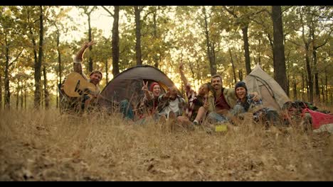 A-happy-group-of-scout-friends-during-a-camping-break-take-a-group-photo-in-hiking-clothes-against-the-backdrop-of-tents-in-an-autumn-green-yellow-forest.-Photo-and-flash-effect