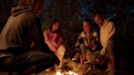 A-company-of-two-boys-and-two-girls-are-roasting-marshmallows-on-a-bonfire.-A-party-outside-the-city.-Rest-in-the-country-house