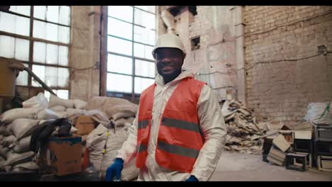 Portrait-of-a-happy-confident-man-with-black-skin-color-in-a-white-uniform-and-orange-worker-at-a-garbage-and-waste-processing-plant.-Male-factory-worker-crosses-his-arms-over-his-chest