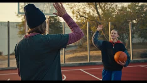 Two-happy-blonde-girls-in-sportswear-after-playing-basketball-give-each-other-high-fives-on-the-red-court-on-the-street-in-the-morning.-Happy-end-of-training-and-victory-after-playing-basketball-in-summer