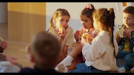 Los-Niños-En-Edad-Preescolar-Se-Sientan-En-El-Suelo-Sobre-Cojines-Especiales-Y-Comen-Manzanas-Y-Plátanos-Durante-El-Recreo.-Durante-El-Almuerzo-En-Un-Club-Preescolar