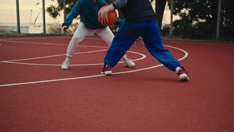 Close-up-shot-of-two-girls-playing-basketball-on-the-red-basketball-court-and-one-of-them-trying-to-throw-the-ball-into-the-basketball-hoop-in-the-morning-during-training