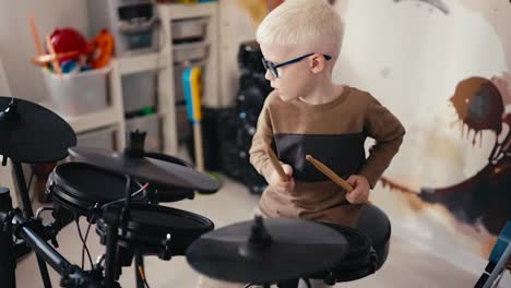 A-small-talented-albino-boy-with-white-hair-in-round-blue-glasses-energetically-plays-on-an-electronic-music-installation-using-wooden-sticks-during-his-weekend-rest-and-development-of-his-talent-and-hobby