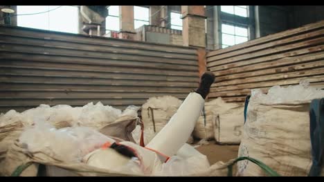 A-brunette-man-in-a-white-protective-uniform-in-a-safety-helmet-and-an-orange-vest-jumps-into-a-large-pile-of-recycled-plastic-cellophane-at-a-waste-processing-and-sorting-plant