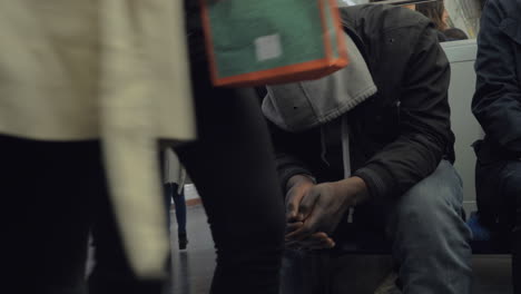 Homeless-man-in-subway-train-hiding-face-under-the-hood