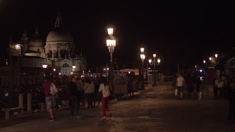 Vista-De-La-Calle-Gente-Y-La-Catedral-De-Santa-María-Della-Salute-En-Venecia-De-Noche