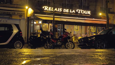 Regnerische-Abendstraße-Mit-Geparkten-Autos,-Motorrädern-Und-Straßencafé