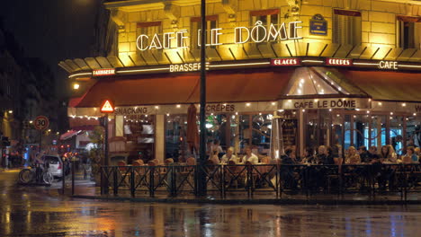 Calle-Parisina-Con-Gente-En-La-Cafetería-Con-Vista-A-La-Noche-Lluviosa.