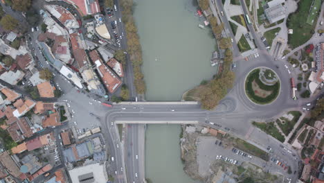 Top-down-aerial-timelapse-of-a-bridge-that-crosses-the-Mtkvari-River-in-Tbilisi,-Georgia