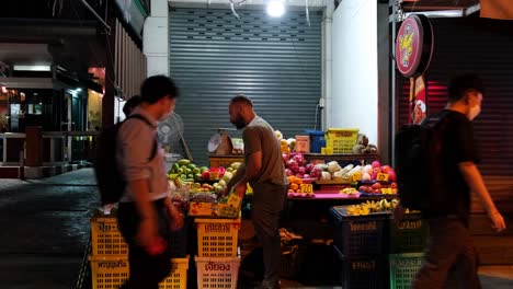 Hombre-Comprando-Algunas-Frutas-De-Un-Vendedor-De-Frutas-En-La-Acera-En-Bangkok-Durante-La-Noche,-Tailandia