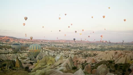 Hot-air-balloon-floats-over-red-valley-rocky-landscape-pan-shot